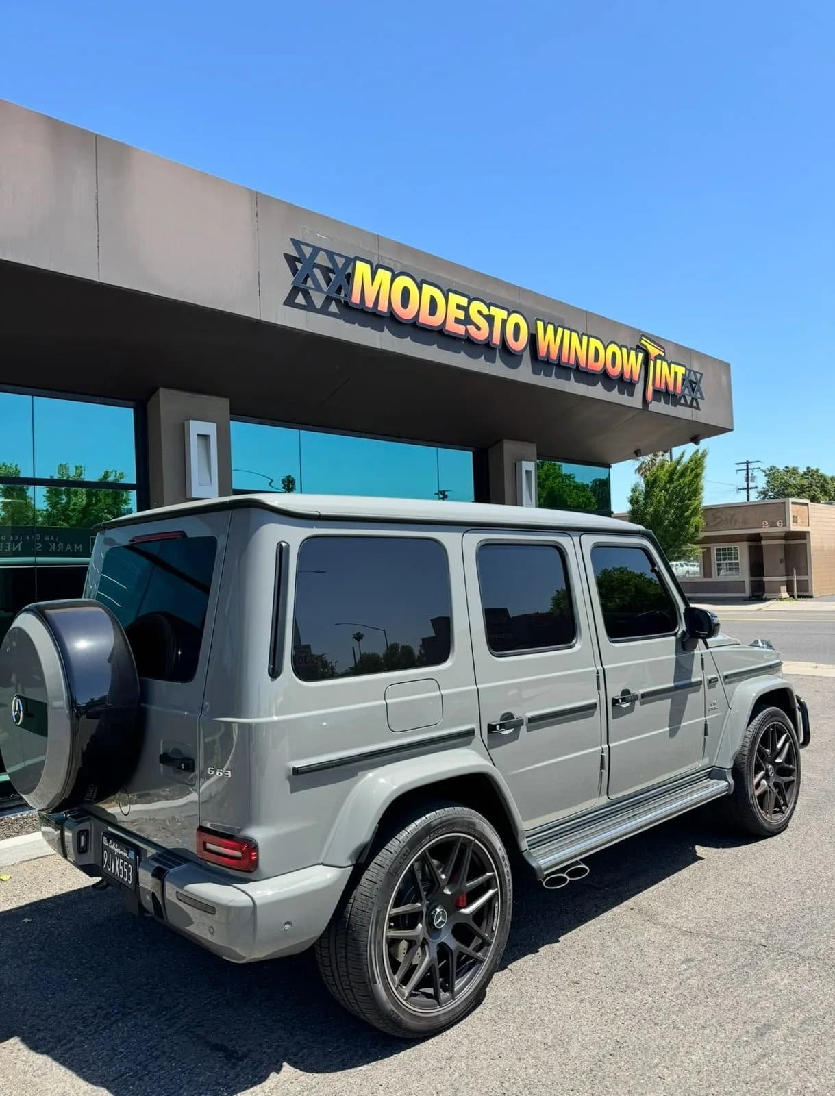 Grey Mercedes G-Wagon with professional window tinting in front of Modesto Window Tint storefront