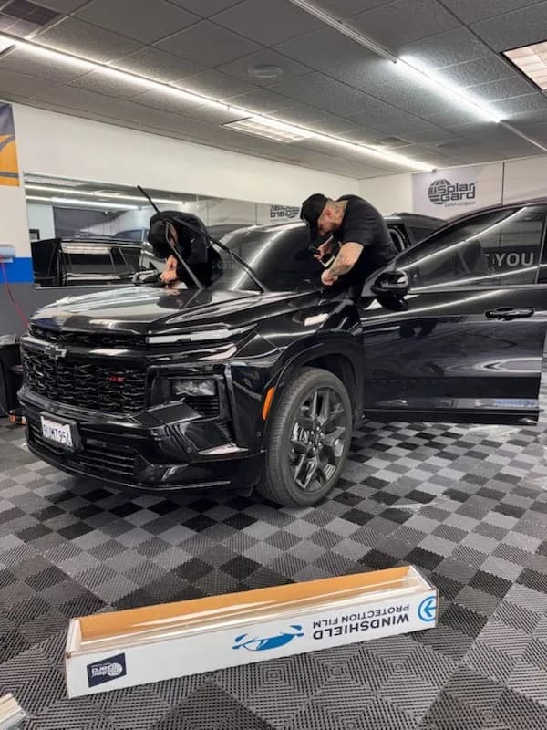 Two expert technicians installing windshield protection film on black SUV