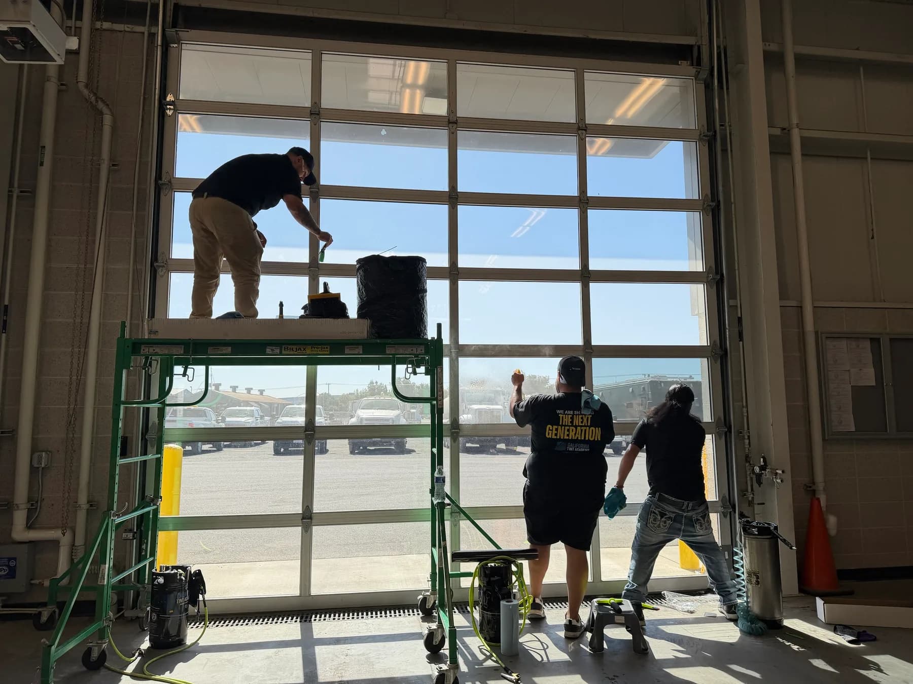 Three installers applying commercial window film to a full-view glass bay door at a Stanislaus County government facility