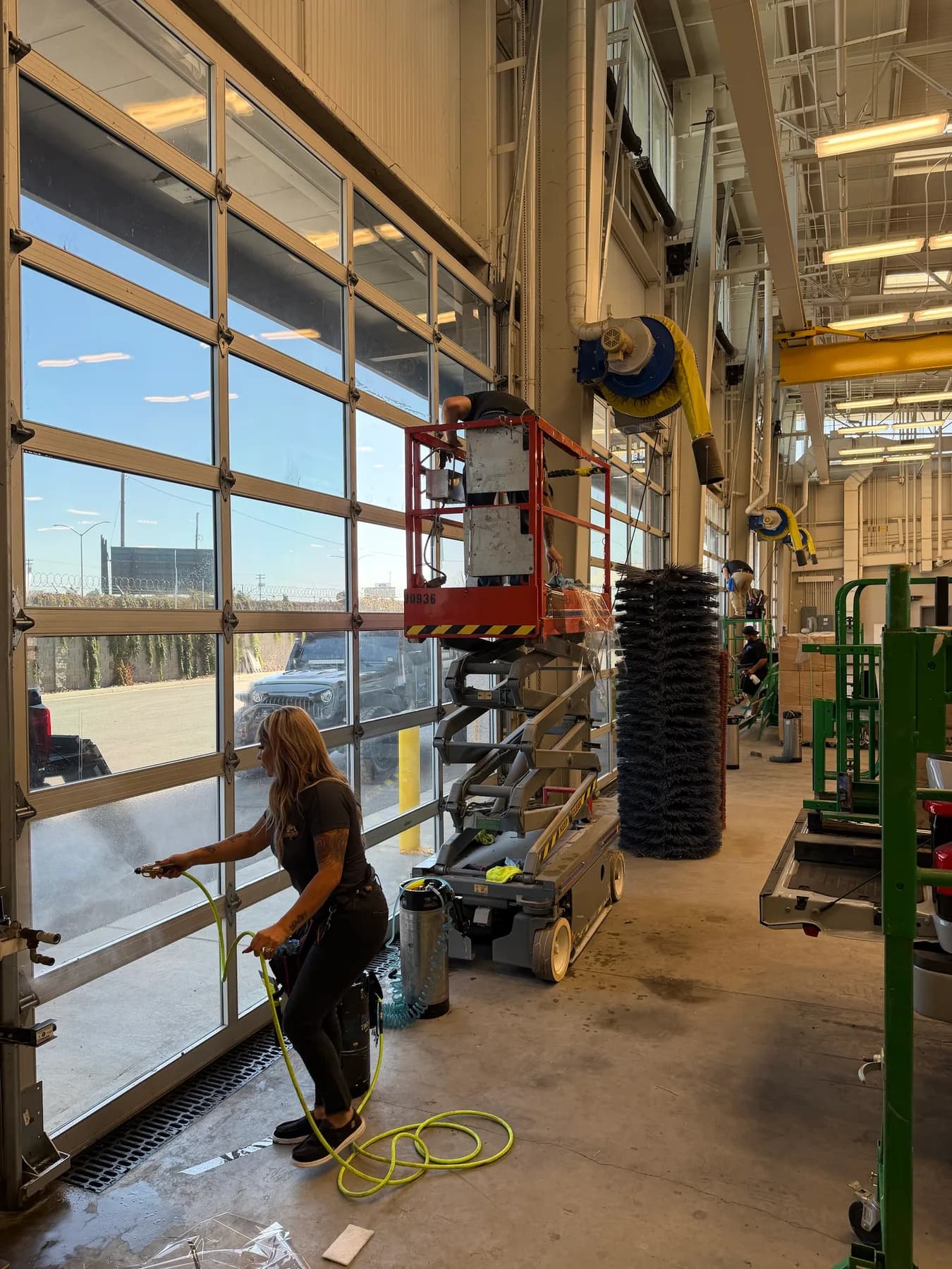 Installer wetting the glass of a roll-up bay door with a pressurized sprayer before applying window film in Modesto